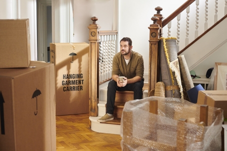 Man sitting on stairs surrounded by moving boxes, representing the decision to move out of the marital home during divorce.