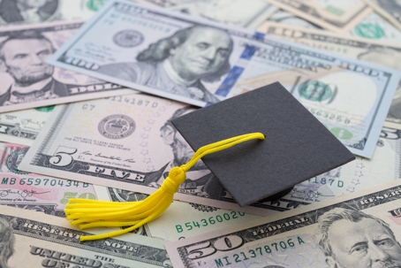 Graduation cap resting on U.S. dollar bills, symbolizing student loan debt and financial considerations during divorce.